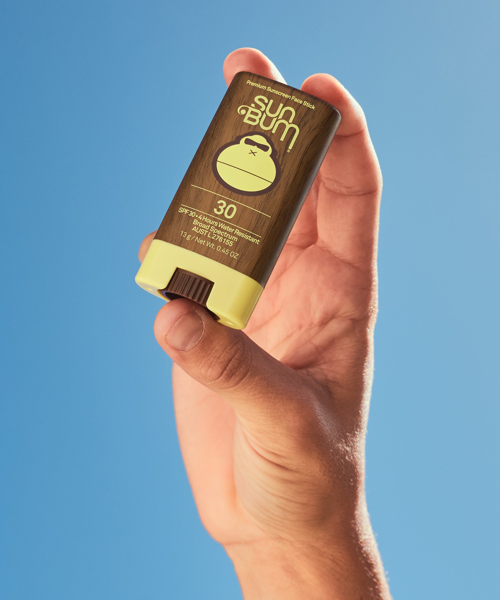 Hand holding a Sun Bum sunscreen stick against a blue background