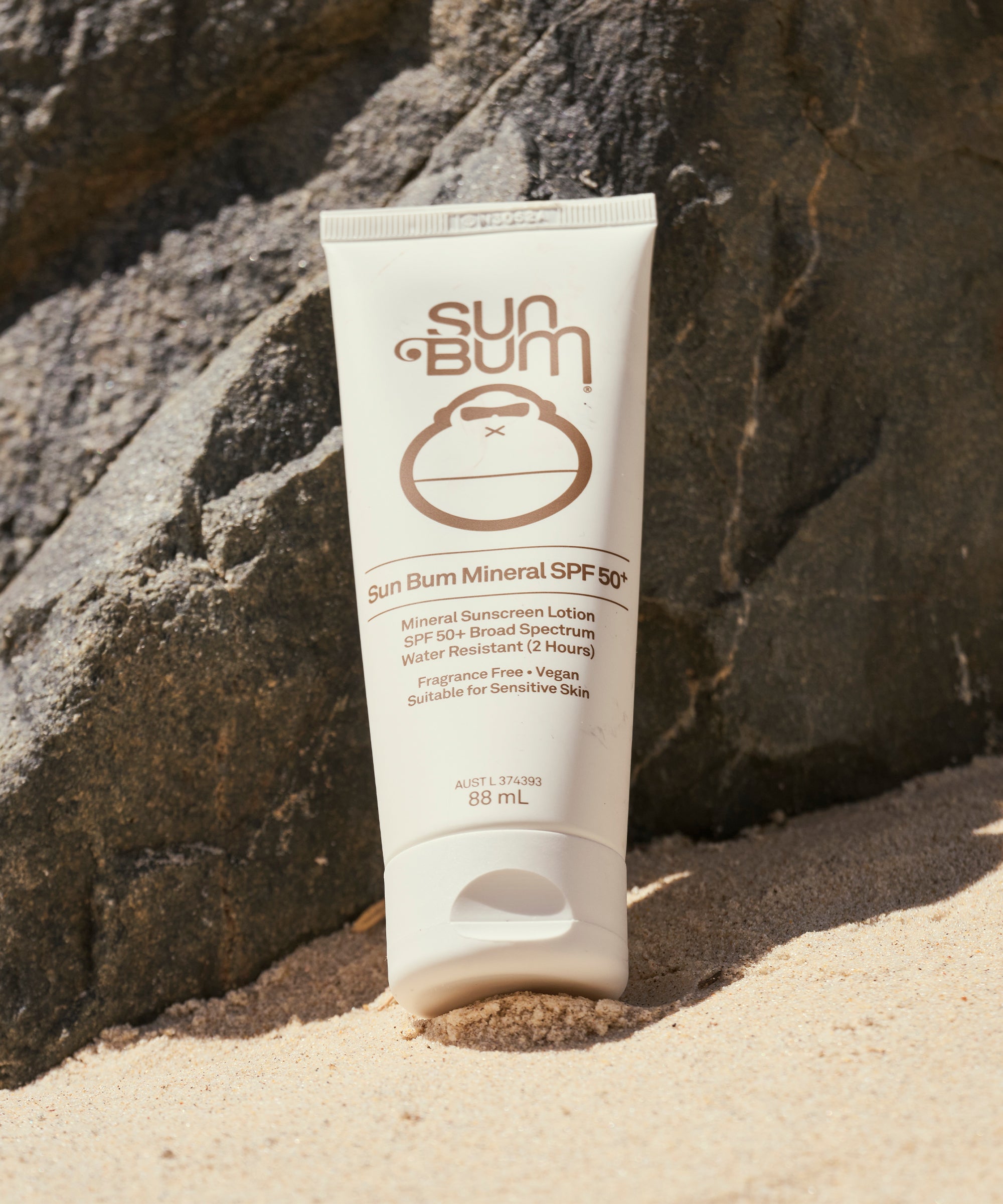 Sun Bum sunscreen tube on sand with rocks in the background