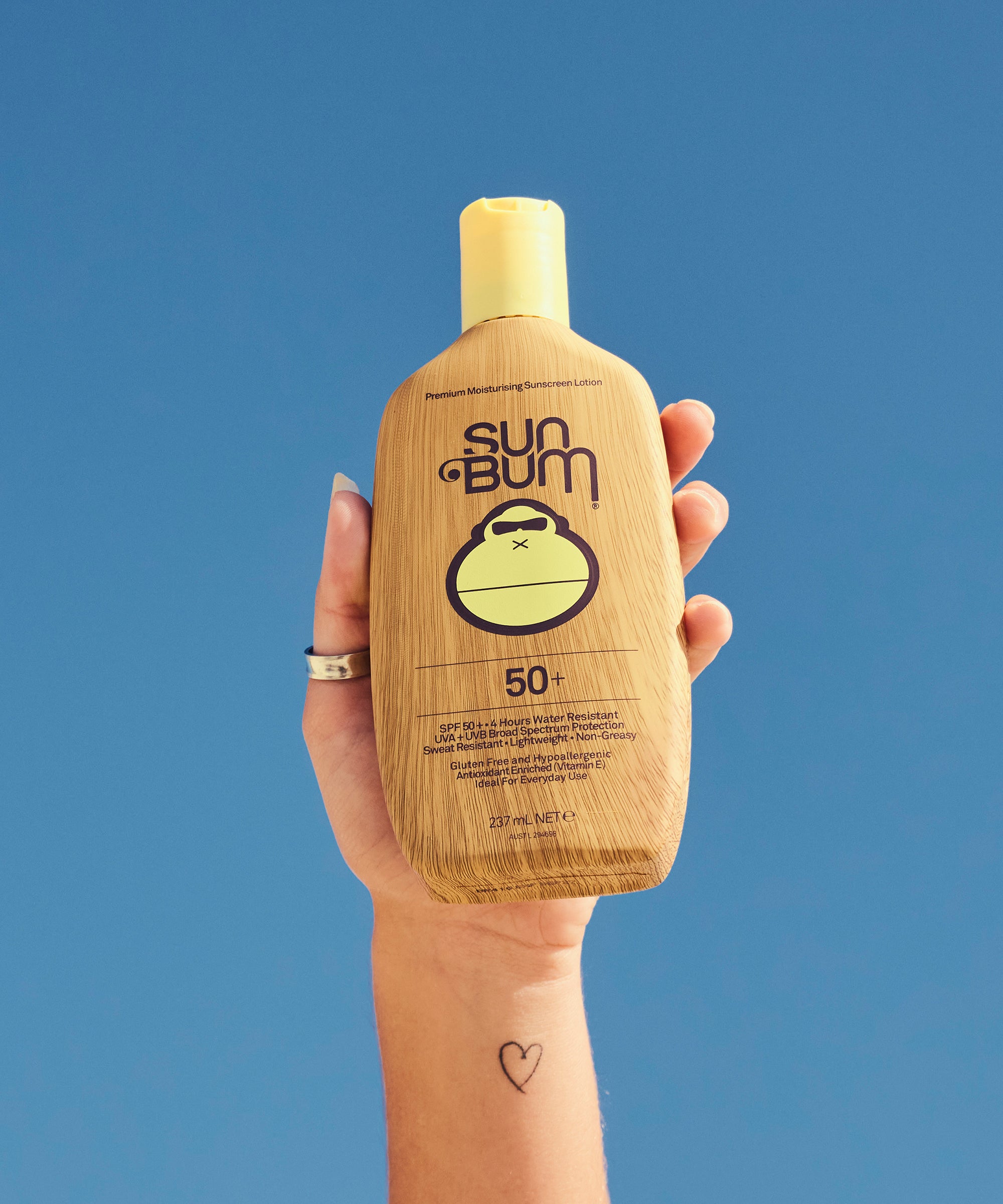 Hand holding a Sun Bum sunscreen bottle against a blue background