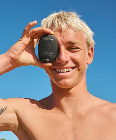 Man holding a black device with '40' on it against a clear blue sky