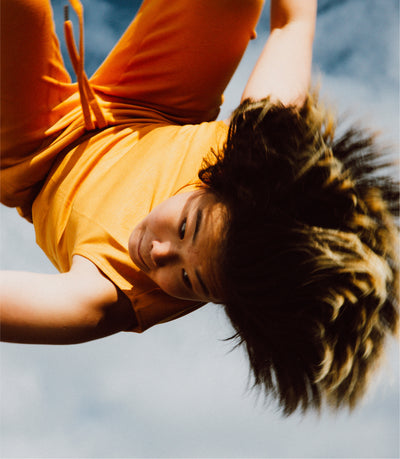 Person in orange shirt upside down against a blue sky