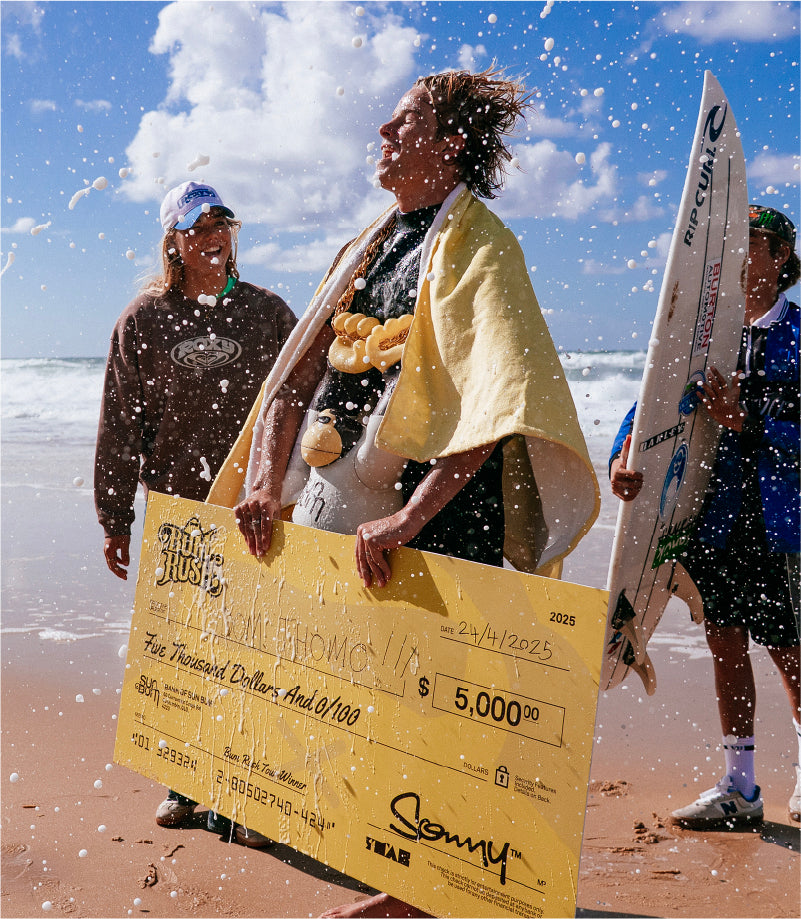 Person holding a large check on a beach with others in the background