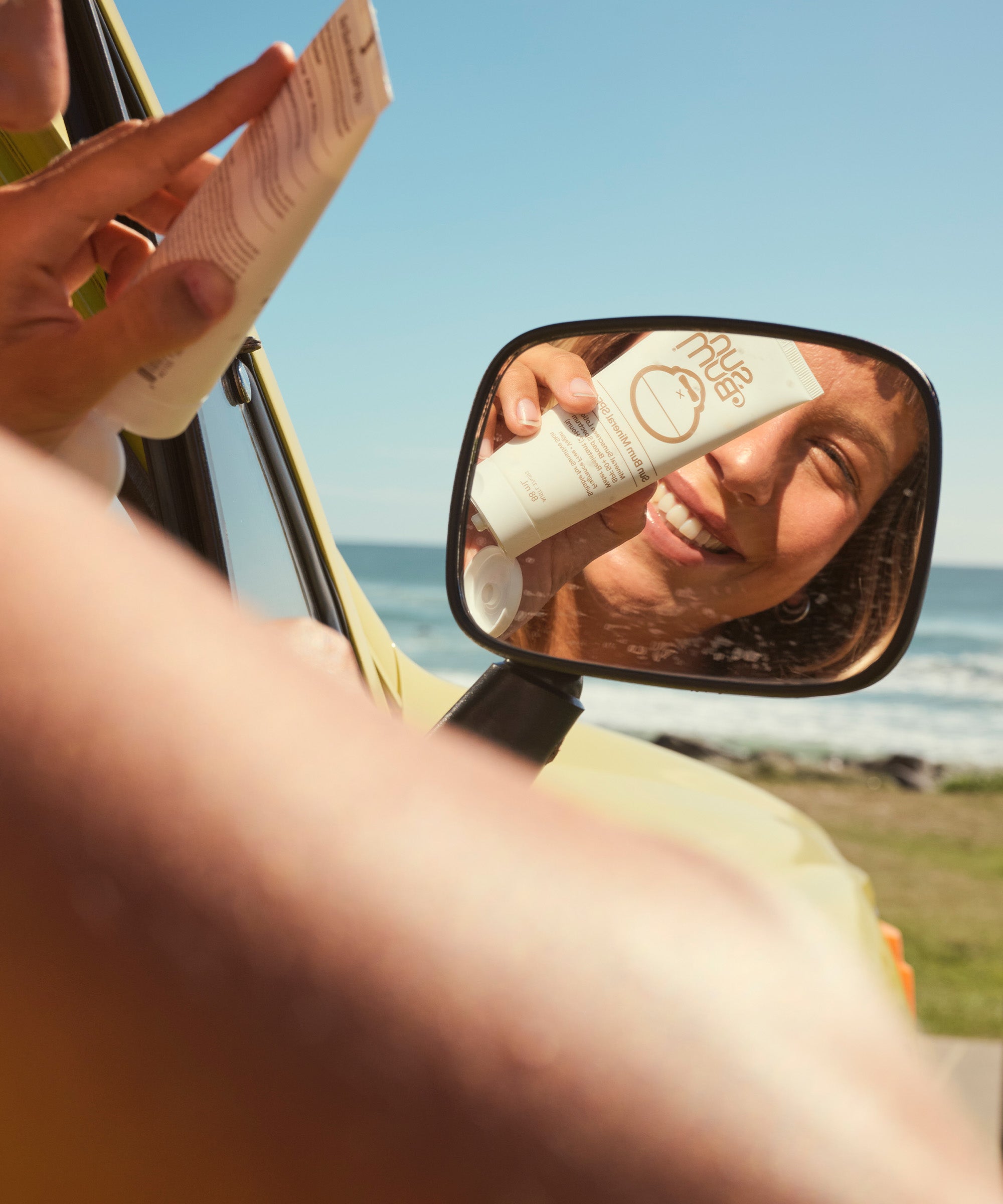 Person applying sunscreen with a mirror reflection by the ocean