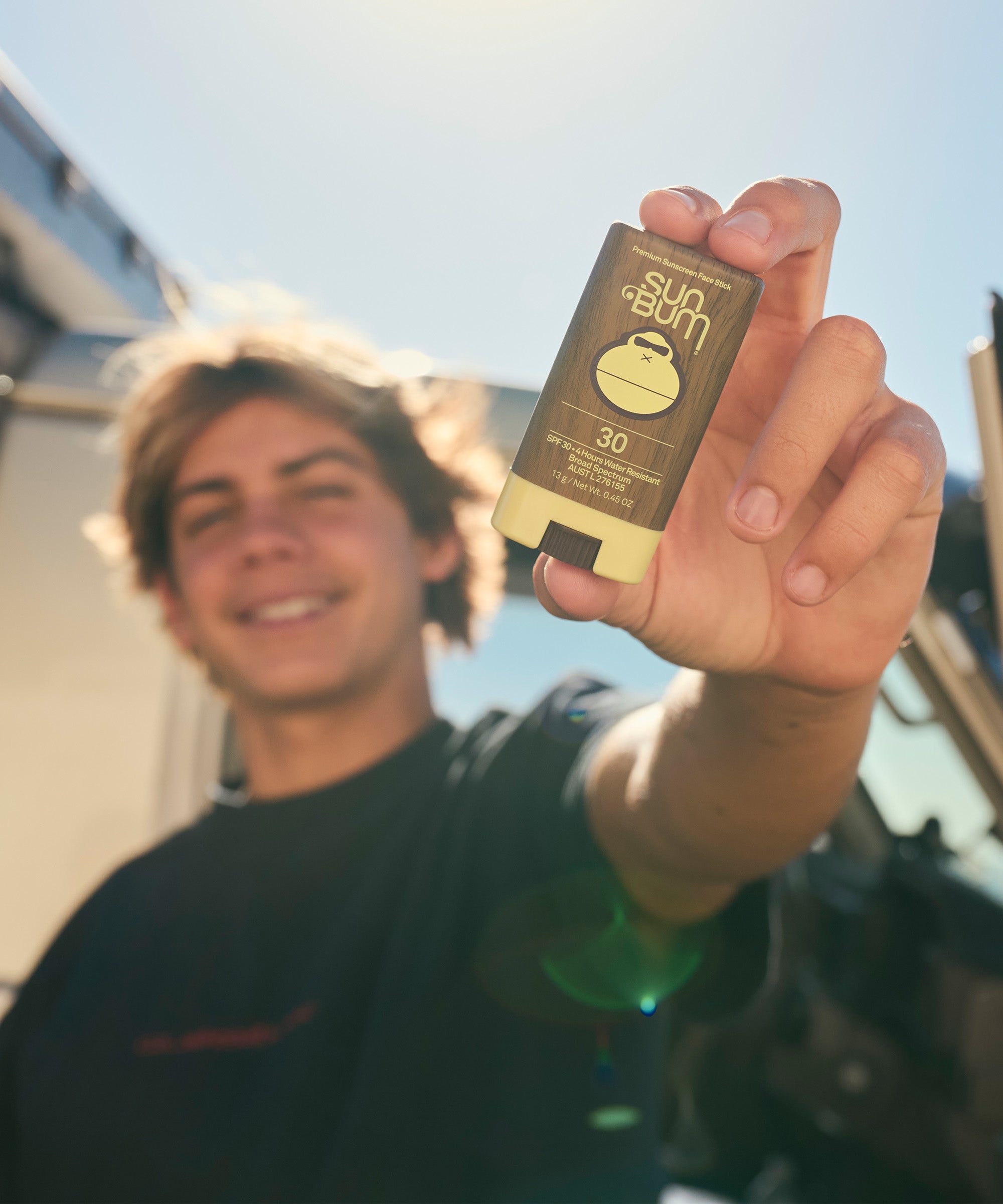 Person holding a Sun Bum sunscreen stick outdoors
