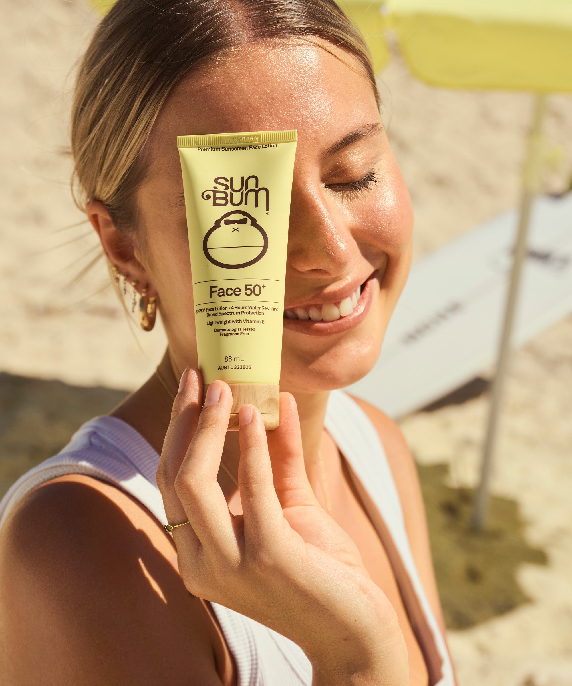 Woman holding a Sun Bum Face SPF 50 sunscreen tube on a beach.