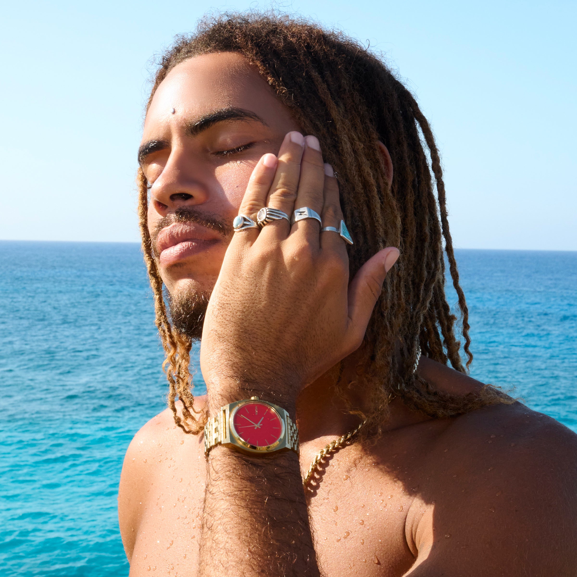 Man with dreadlocks and a red watch against a blue ocean background