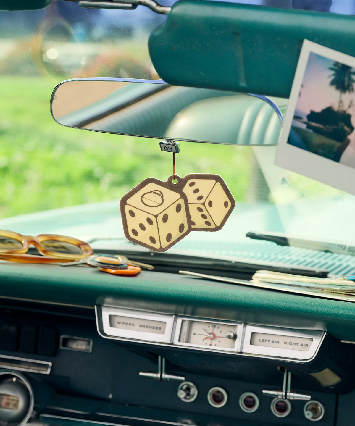 Vintage car interior with dice-shaped ornament, sunglasses, and a photo on the dashboard.