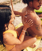 Woman applying Original SPF 30 Sunscreen Lotion on a man’s back at the beach. Sun Bum.