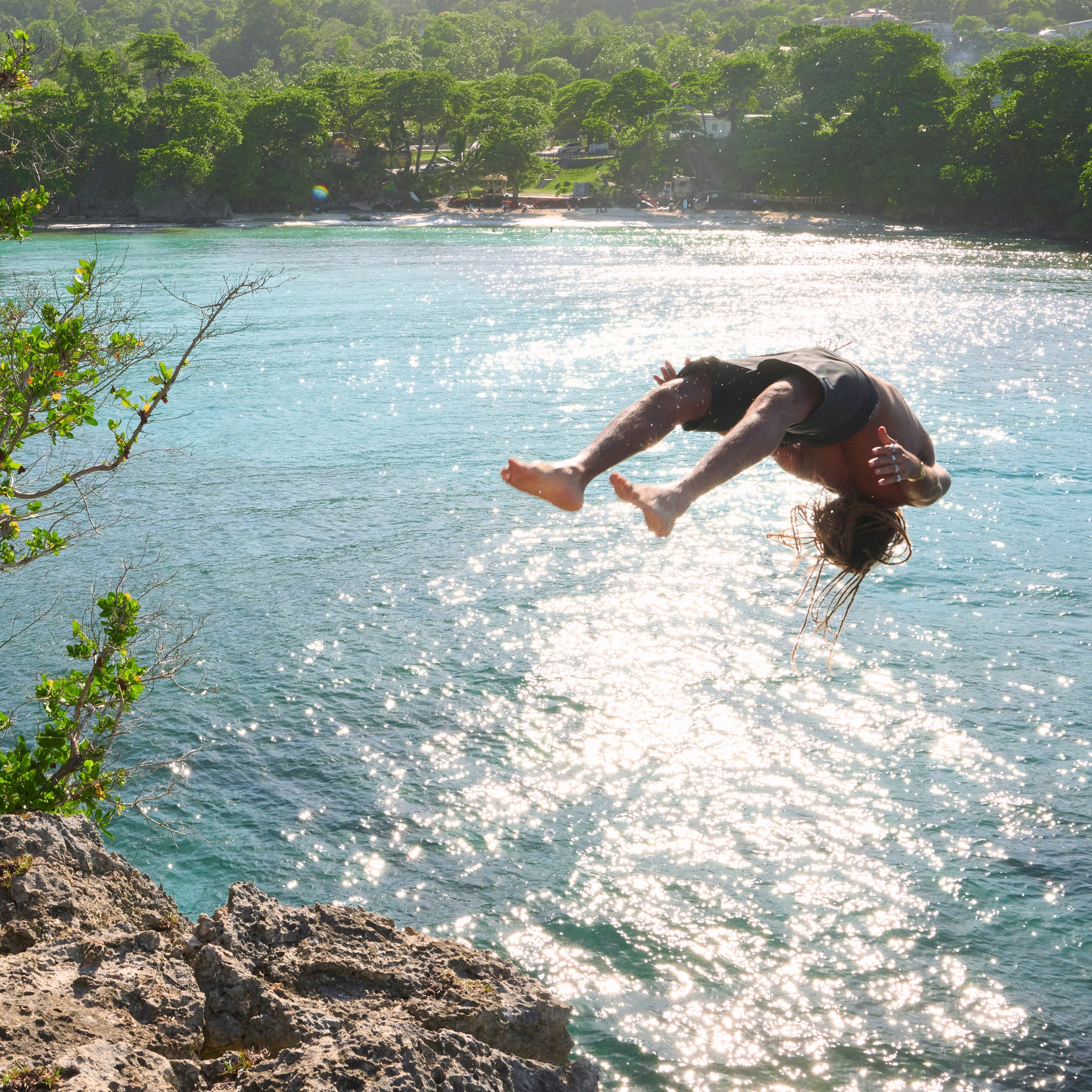 Person diving into a body of water from a cliff with trees in the background