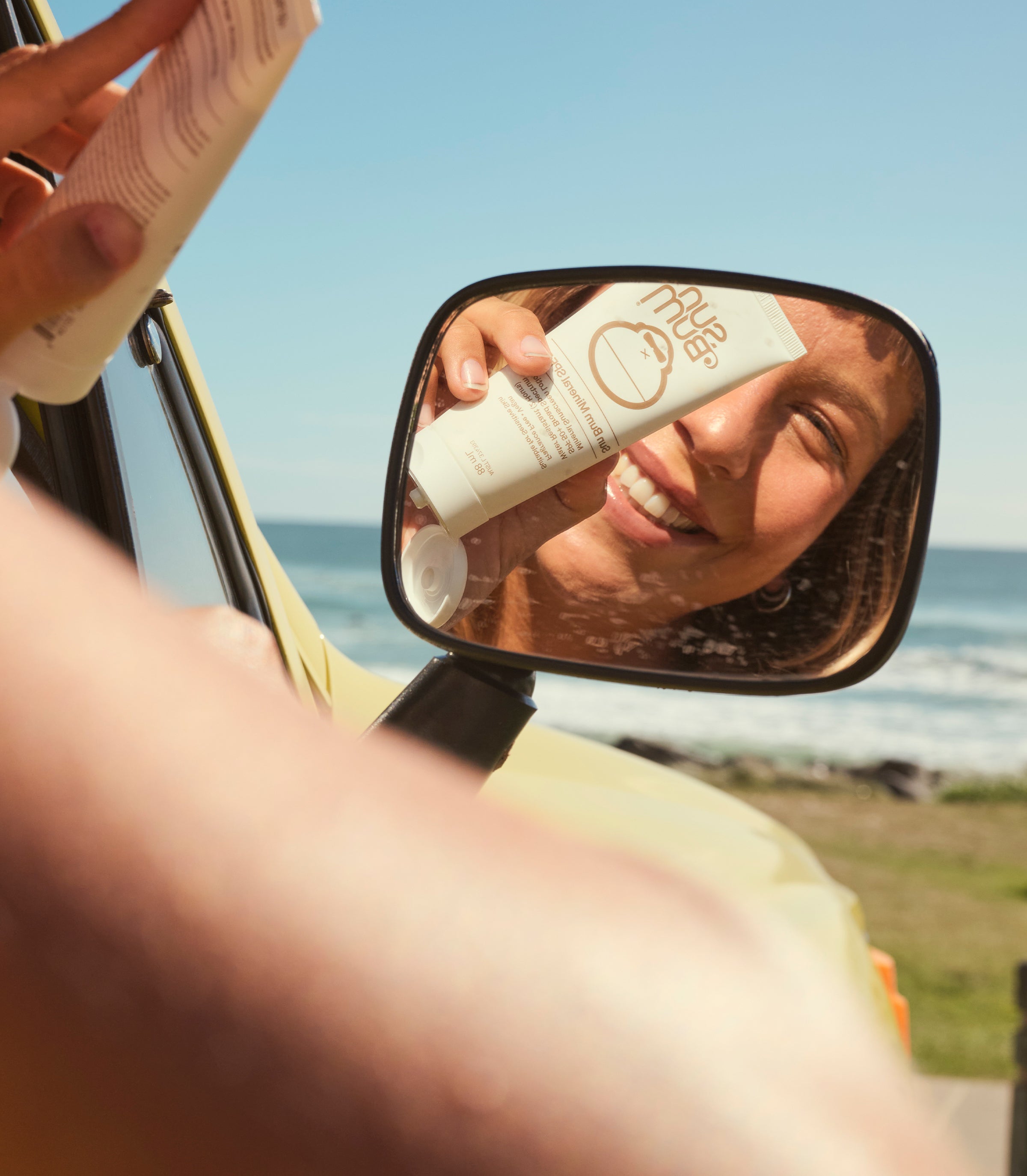 Person applying sunscreen with a mirror reflection by the ocean