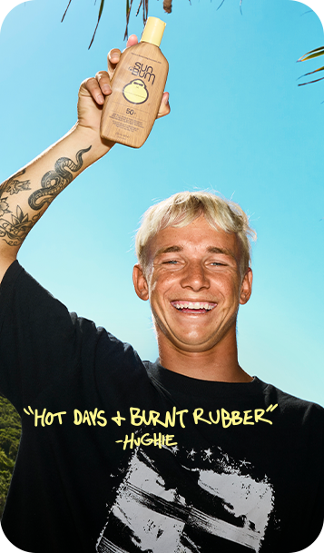A smiling man outdoors against a bright blue sky holds up a bottle of Sun Bum sunscreen. He wears a black graphic T-shirt with yellow text that reads, "HOT DAYS + BURNT RUBBER" -HIGHIE.