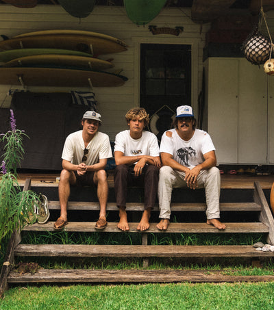 Three friends sitting on a porch surrounded by surfboards and tropical vibes, featured in the Discover Blog Collection - Sun Bum.