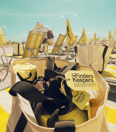 Close-up of Sun Bum beach tote with towel and merch on a sunny beach, part of the Finders Keepers surprise giveaway – Discover Collection - Sun Bum.