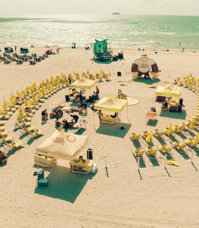 Beach scene with yellow umbrellas and tables arranged in a circular pattern on a sandy beach.