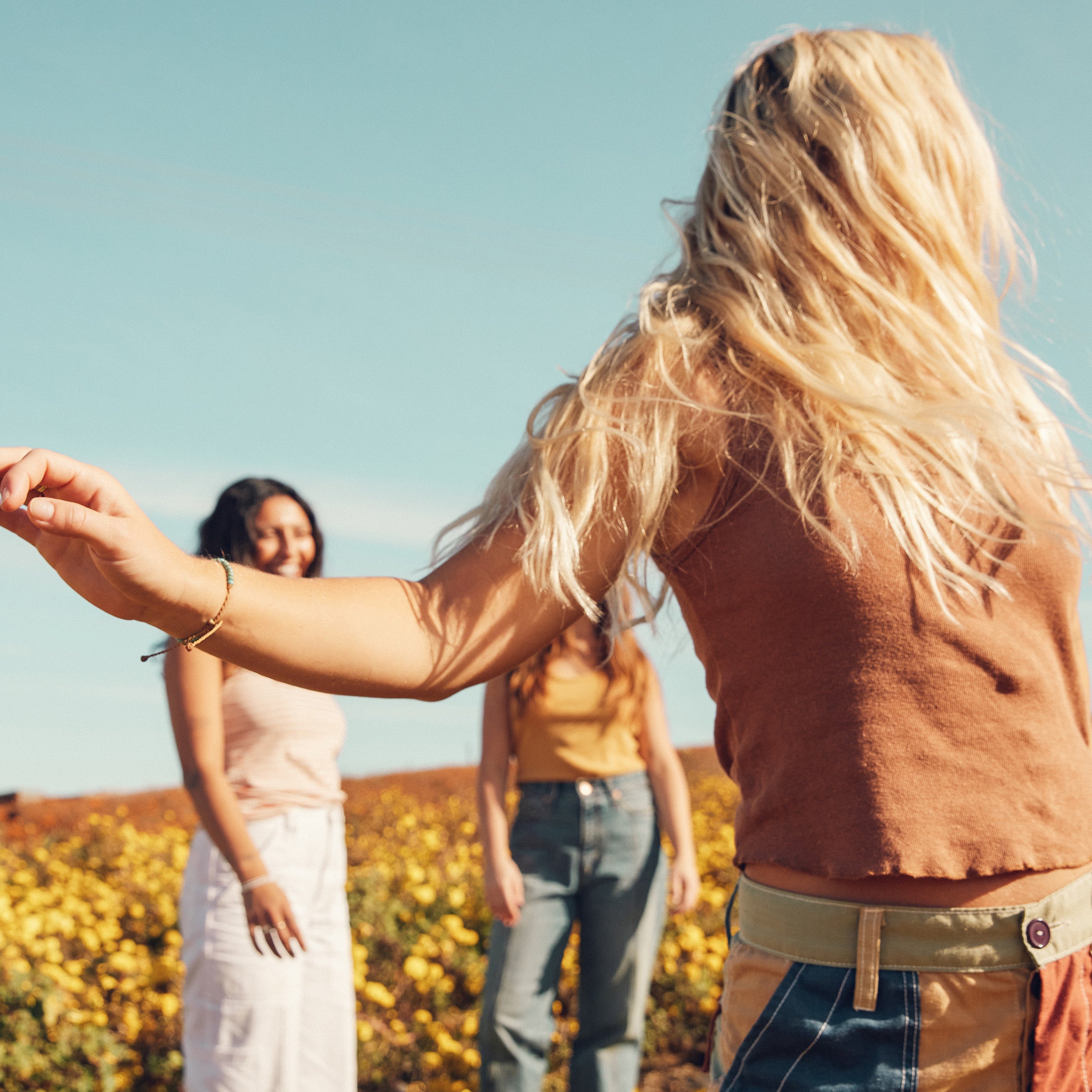 Friends dancing in a sunny flower field, highlighting vibrant blonde hair care – Blonde Collection - Sun Bum.
