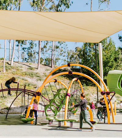 Kids and parents enjoying a shaded playground with modern equipment, highlighting PTG Sun Education Collection - Sun Bum.