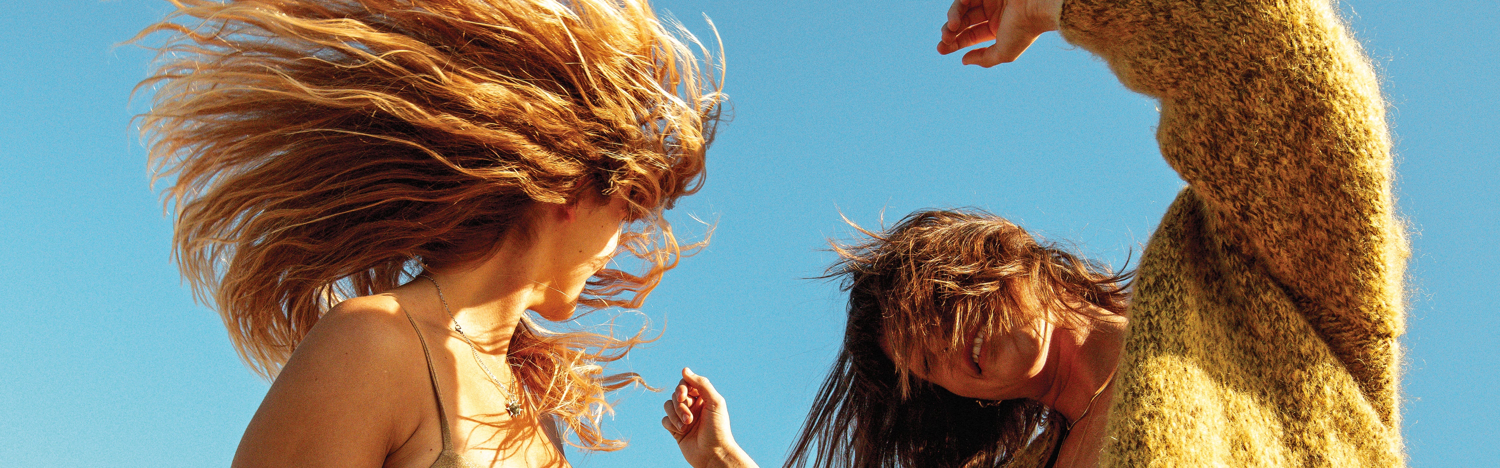 Two girls dancing in the wind with their beachy hair looking fun and free. - Sun Bum