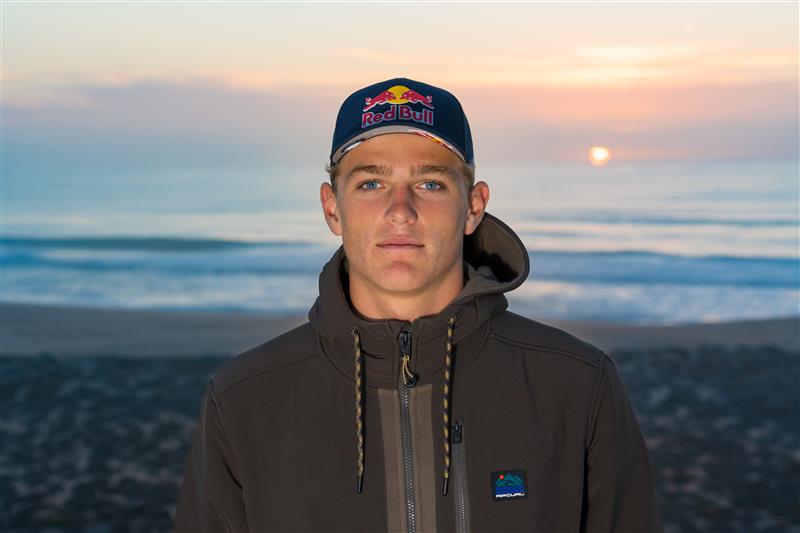 Person wearing a Red Bull cap with a sunset over water in the background