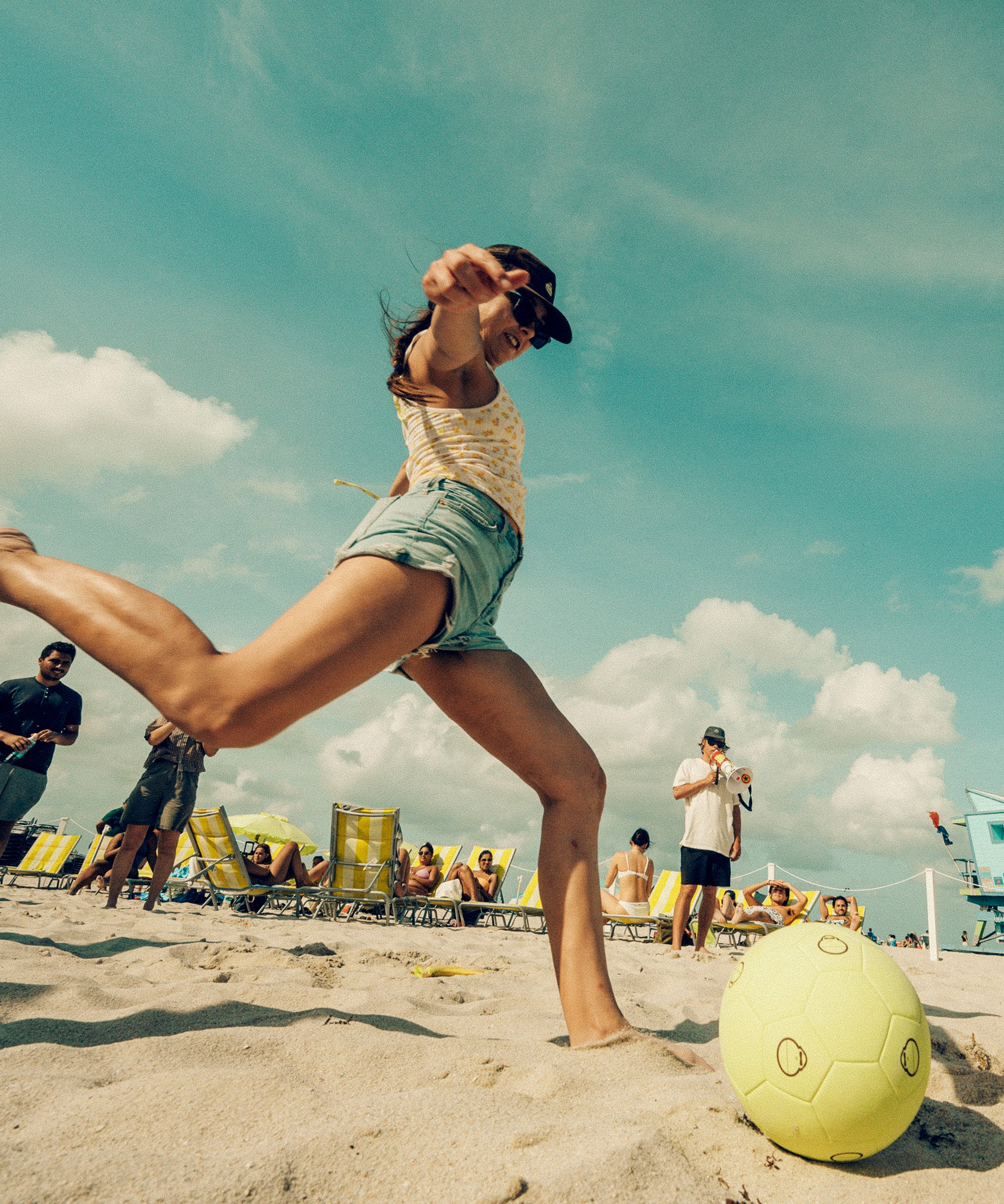 Woman playing with a yellow ball on a beach with people in the background